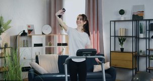 Likable smiling happy fit young sportwoman training on running track at home and talking with friend via video call,healthy lifestyle and modern technology concept