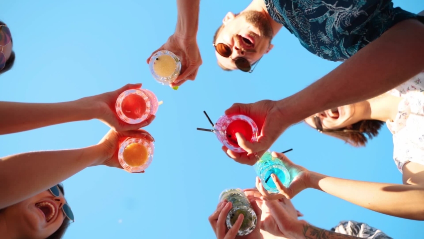 Low angle view of friends having fun at pool party, clinking glasses with colorful summer cocktails near hotel swimming pool. People toast drinking fresh juice at luxury summer villa in slow motion. | Shutterstock HD Video #1072401590