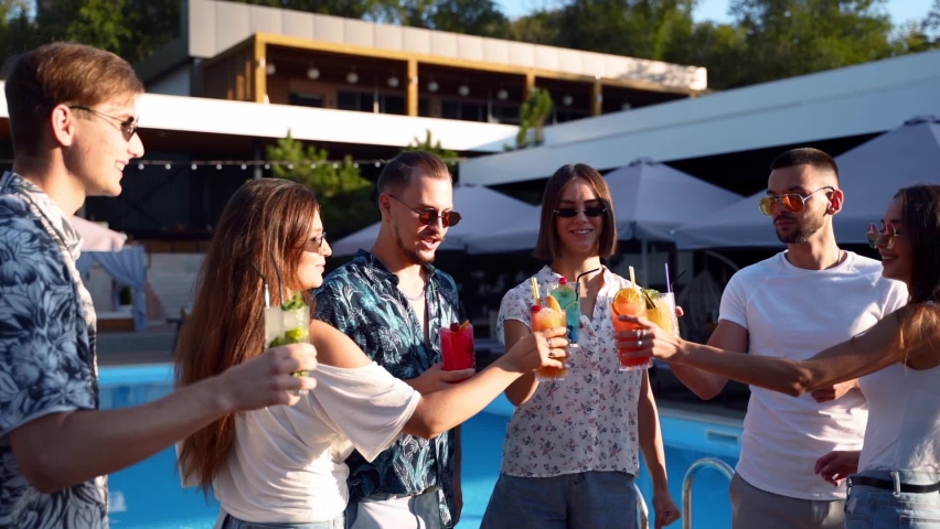 Group of friends having fun at poolside summer party clinking glasses with summer cocktails on sunny day near swimming pool. People toast drinking fresh juice at luxury tropical villa in slow motion. | Shutterstock HD Video #1072401602
