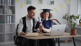 distance learning, cheerful young couple in academic clothes celebrating graduation ceremony and diploma by video link on laptop