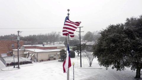 Rotating shot of the USA flag and the Texas flag blowing in the wind along with the snow flurries.