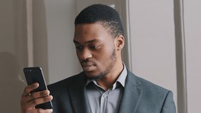 Frustrated African American guy look at cell phone screen reads bad news in mobile message concept, feels shocked. Worried businessman lost money thinking over sudden problems after reading sms