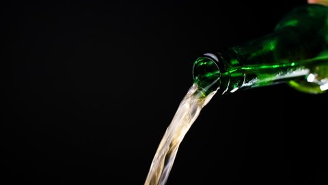 Stream of beer runs through the open green glass bottle in slow motion video, cold beer pours out, liquid flows, beverage tabletop, alcohol drink