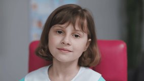 Funny little girl looking at camera are sitting on the couch at home. Cute kid child with pretty face. Concept of a happy childhood. Portrait of girl in medic uniform looking at camera in slow motion