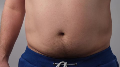 Close-up of a male fat shaking belly against a white background. The obese man touches his stomach and shows his thumb down