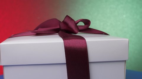 Decorative anniversary present box with purple ribbon and bow on blue table against green and red wall zoom out panorama. Concept celebration