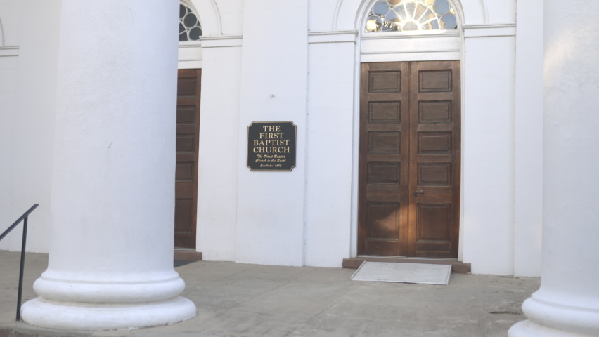 Big white columns outside the First Baptist Church in Charleston, South Carolina. Commemorative plaque, wooden doors, clean white walls on facade of American church. Architecture and religion