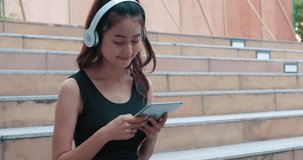 Beautiful satisfied slender fit girl in black sport clothes relaxing on the stadium and enjoying nice songs in headphones from her phone playlist after workout
