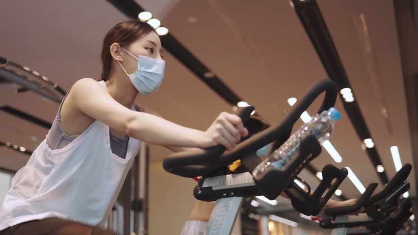 Young  asian female  in sport wear outfit in gym  with medical protective mask. Coronavirus COVID-19 quarantine. Fitness and healthy lifestyle concept. Side view of girl in sportswear . Royalty-Free Stock Footage #1072438100