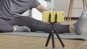 Young Woman Doing her Daily Stretch Routine. Young woman stretches her legs as shown on her video fitness training