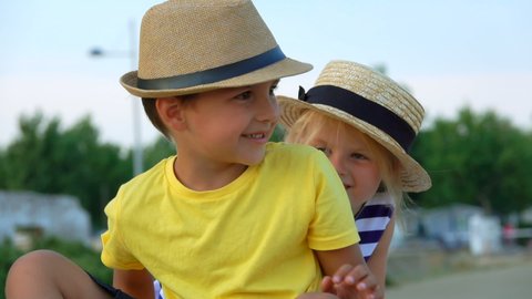 Little boy and adorable blond girl in hats are looking at the camera outdoors