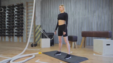 Sporty Blonde Woman Doing Sports Doing Exercise Squats, Dressed in Sporty Black Clothes, Light Gym