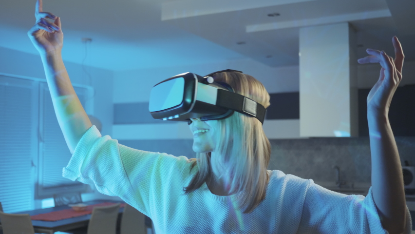 Middle shot of a Caucasian woman with VR glasses watching a virtual simulation of a concert and light show, dancing with arms up and swinging in the rhythm of the music Royalty-Free Stock Footage #1072444331