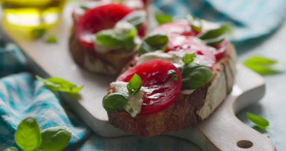 Pouring olive oil over caprese sandwiches based on sourdough bread with the addition of tomatoes, mozzarella cheese and fresh basil  on a white board close up view Royalty-Free Stock Footage #1072460813