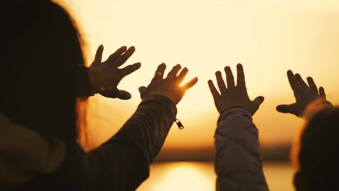 Silhouette of reaching, helping hand, hope and support each other over sunset. People hands reaches for the sky and closes the sun, the sun's rays pass through the hand.