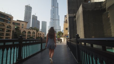 Woman walking in luxury tourist resort by the Burj Khalifa skyscraper in Dubai. Tourist walking around luxury apartment complex and restaurants by the pool in Dubai, UAE in 2021