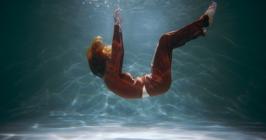 Cinematic side view of young beautiful woman slowly sinking deep under water. Depression, loneliness concept slow motion