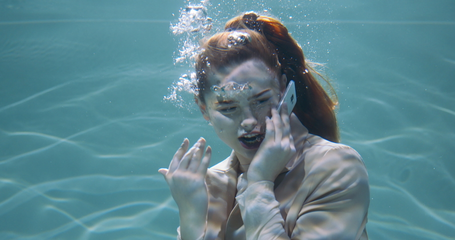 Cinematic under water portrait of angry stressed young redhead business woman shouting talking on phone call slow motion