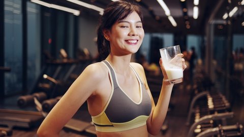 fitness center give protein shake to young slim beautiful woman. In sports center redheaded lady with ponytail in black sportswear sitting at wooden bar, drink nutrition milk .