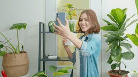 Happy young woman taking selfie with her plants and making video call at home 