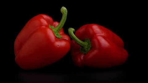 Video of two red bell peppers slowly turned on a Black background.