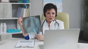 Female medical doctor wears white coat, headset video calling distant patient on laptop. Doctor talking to client using virtual chat computer app. Telemedicine, remote healthcare services concept