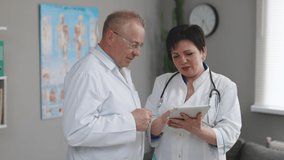 Medical team two old male and young female doctors wear white coats talk, use digital tablet. Two Hospital Partnership in medicine concept, healthcare tech. - Powered by Shutterstock - Get 15% off with code: PIKWIZARD15