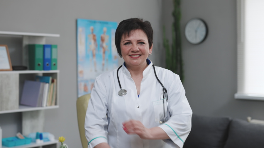 Happy european woman doctor wearing white medical coat and stethoscope looking at camera. Smiling female physician posing in hospital office. Positive general practitioner portrait. Royalty-Free Stock Footage #1072473638
