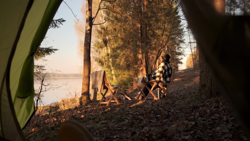 A young girl on a picnic with a tent fries marshmallows over the fire and drinks coffee.