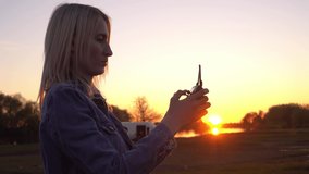 a woman holds a remote control drone at sunset close-up. The woman moves the sticks and controls the drone and the camera. Beautiful young blonde in a denim jacket. Summer.