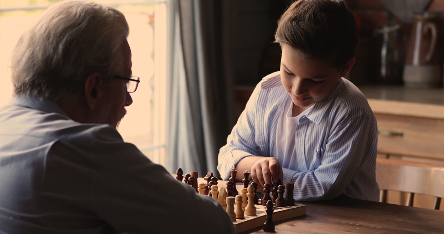 Grandpa and little grandson play chess sit at table. Multi-generational family engaged in educational board game. Kid development, improve concentration, gain abstract thinking skills, hobby concept Royalty-Free Stock Footage #1072477985
