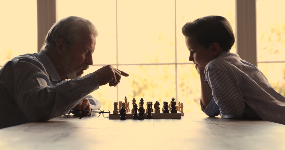 Older grandpa and little 7s grandkid play chess sit at table at home. Small boy aged grandfather spend time together talking making moves enjoy board game. Leisure activity, hobby, brain work concept Royalty-Free Stock Footage #1072478108