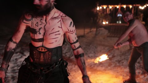 Battle an evil aggressive viking warrior in northern tattoos with a bare torso on burning fire swords with an opponent from our days wearing glasses