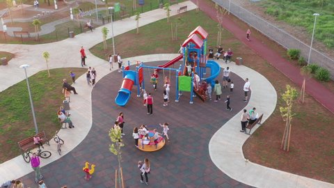 Playground for kids in a park, busy with excited and joyful children having fun and playing on merry-go-round, slide, playhouse and swing and running around. Podgorica Montenegro May 11.2021.