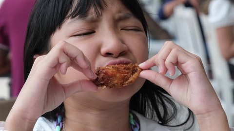 Asian child girl in a white shirt is eating fried chicken with deliciousness.
