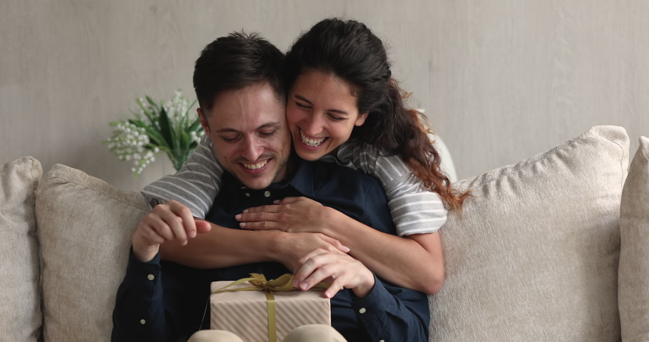 Happy husband receive gift box from loving wife. Woman in love cover eyes, hug from behind beloved man prepare surprise congratulates birthday, anniversary, express care, show attention at special day Royalty-Free Stock Footage #1072486934