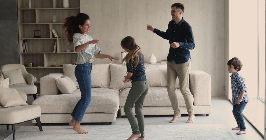 Happy homeowners family dancing barefoot in fashionable living room. Married cheery couple their beautiful active children listen to music funny moving at home, having fun on weekend. Hobby concept Royalty-Free Stock Footage #1072486955