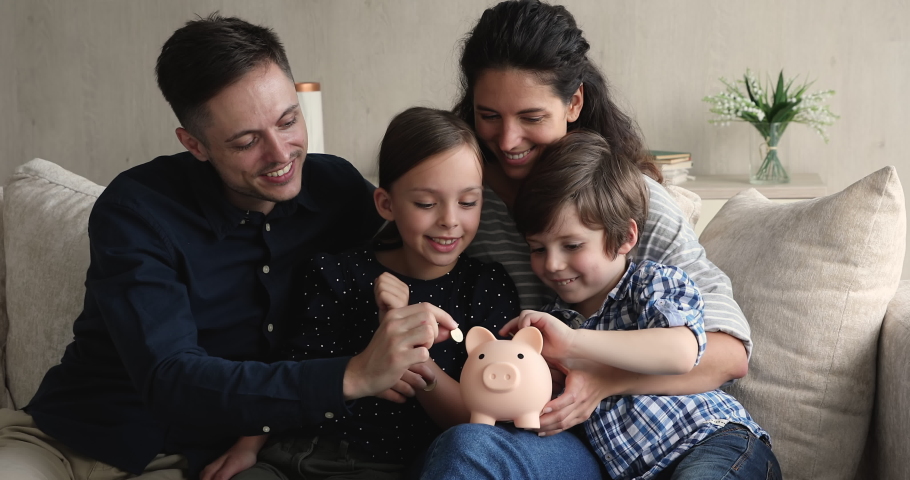 Young couple preschool son little daughter sit on sofa dropping coins into piggy bank. Happy family saving money for new housing, dream, education of children in future. Teach kids be thrifty concept | Shutterstock HD Video #1072493189