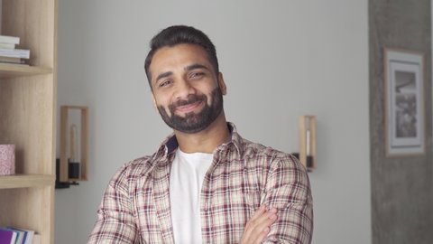 Headshot portrait of attractive confident indian Hispanic man looking at camera standing at modern living room. Latin businessman posing in casual stylish look at home office.