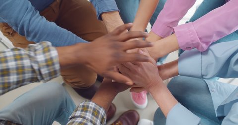 Multiracial people putting hands together in team meeting. Cropped shot of diverse people sitting in circle and joining hands at group support meeting or therapy session
