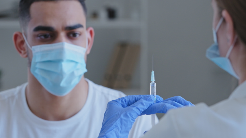 View from behind woman doctor nurse holding syringe with drug vaccine for covid male patient hispanic arab man in mask waves hands no refuses disagrees with vaccination protests against treatment Royalty-Free Stock Footage #1072504976