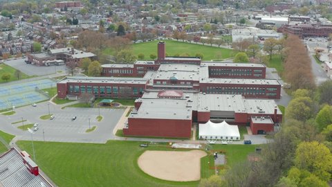 Establishing orbit shot of large USA school building and athletic grounds and baseball field. Urban American educational system theme.