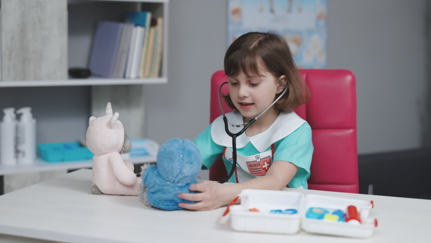 Funny little child girl wear medical uniform holding stethoscope playing game as doctor. Happy cute adorable small preschool kid pretending medic nurse. Royalty-Free Stock Footage #1072527764