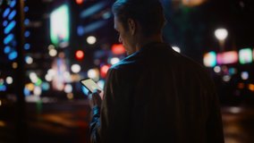 Following Shot of Handsome Man Using Smartphone Walking in a Modern City Street with Neon Lights at Night. Attractive Male Walking Through Urban Area using Mobile Phone. Medium Tracking Cinematic Shot - Powered by Shutterstock - Get 15% off with code: PIKWIZARD15