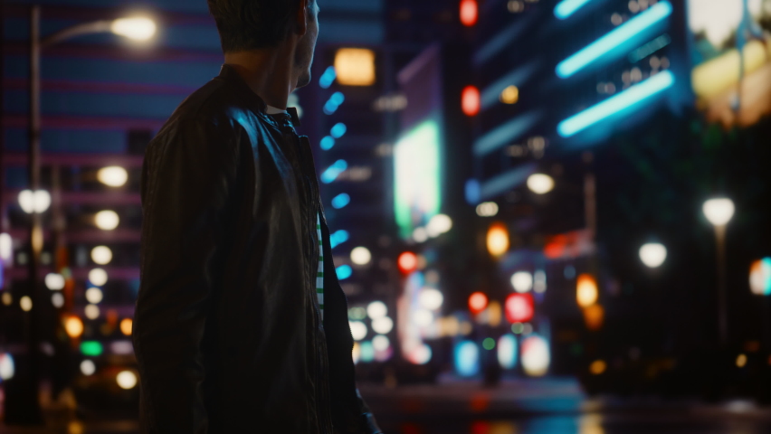 Handsome Young Man Using Smartphone Walking Through Night City Street Full of Neon Lights. Smiling Stylish Blonde Male Using Mobile Phone for Social Media Posting. Profile View Tracking Medium Shot Royalty-Free Stock Footage #1072530275