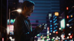 Handsome Young Man Using Smartphone Walking Through Night City Street Full of Neon Lights. Smiling Stylish Blonde Male Using Mobile Phone for Social Media Posting. Profile View Tracking Medium Shot - Powered by Shutterstock - Get 15% off with code: PIKWIZARD15