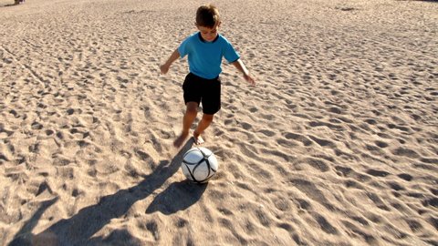 Football soccer game on the beach. Little boy playing with a ball on the sea beach, 4k slow motion