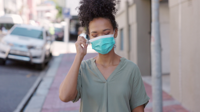 Happy African girl walking outdoor while taking off her protective face mask and looking at camera after immunization from Covid19. We are now safe, coronavirus ended, quarantine is over concept. | Shutterstock HD Video #1072531856