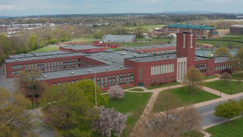 Rising aerial reveals large red brick academic school university building exterior. Outside view in spring by drone.
