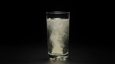 Macro shot of effervescent tablet dissolves with bubbles in pure water isolated black background. Vitamins C pills against flu, medicines, At home treatment.